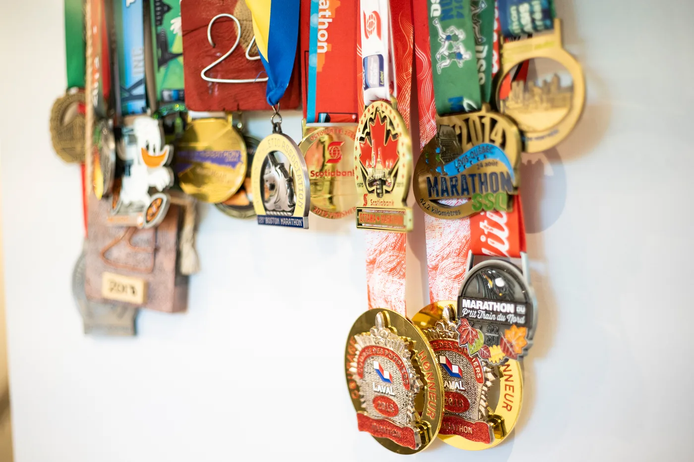 Une rangée de médailles de course suspendues à un support mural, dont plusieurs médailles de marathon de Laval et du Nord