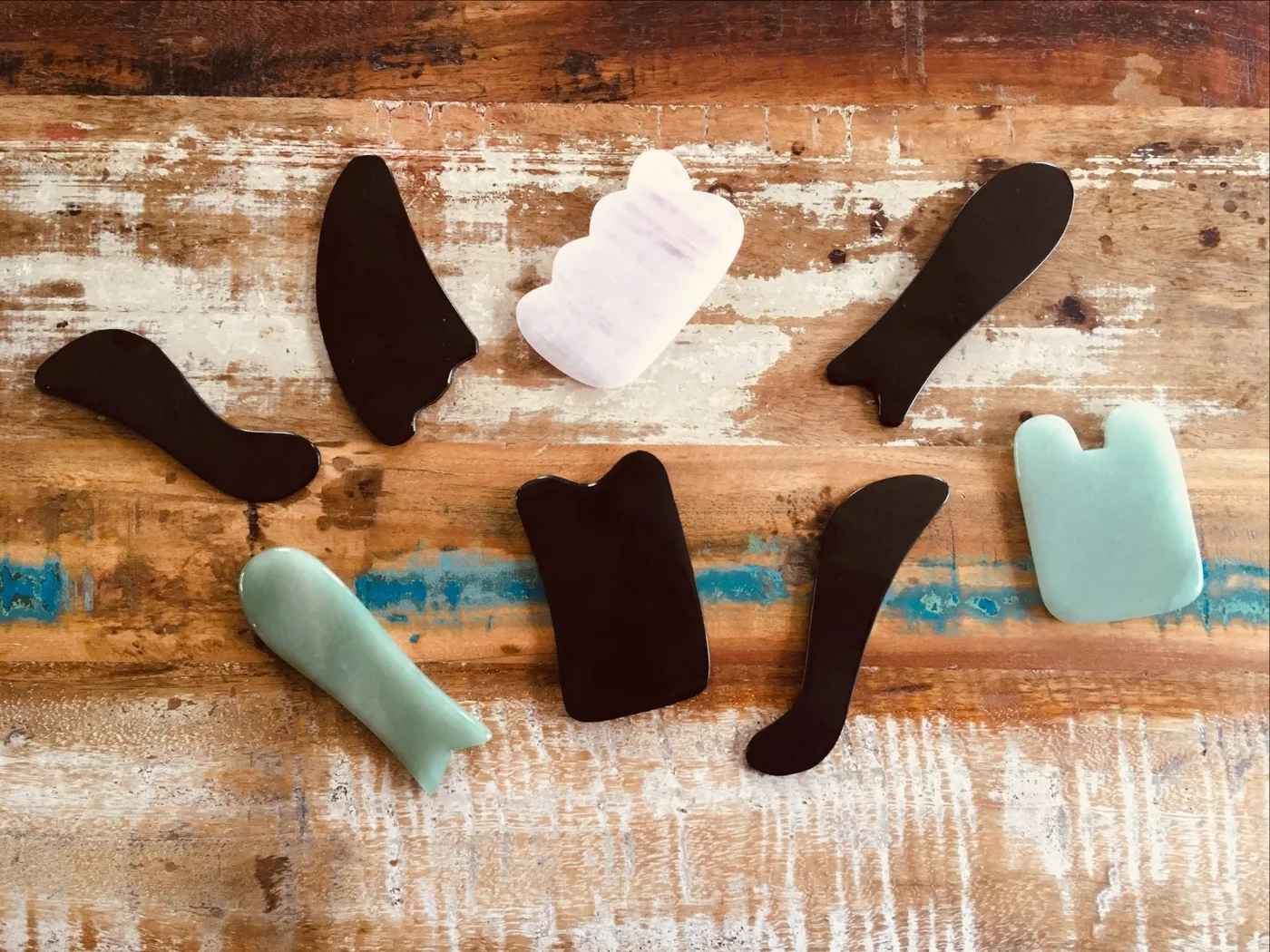 Huit outils de gua sha — noirs, blancs et vert d'eau — disposés sur une planche de bois usé