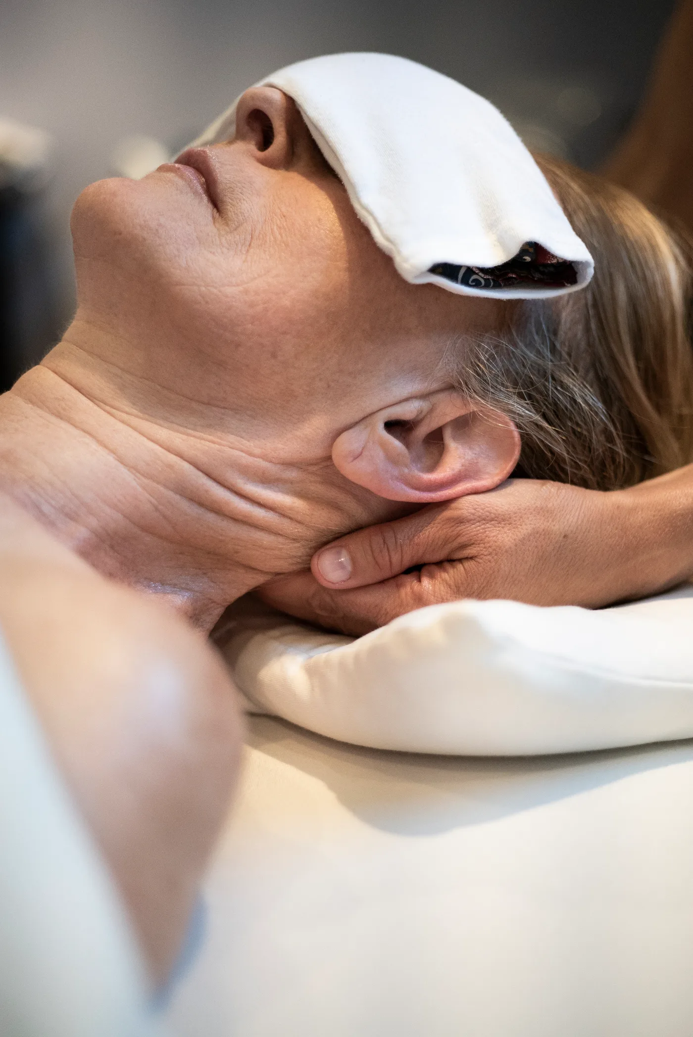 Gros plan du visage d'une femme couchée sur le dos, une compresse blanche posée sur les yeux ; une main soutient sa nuque