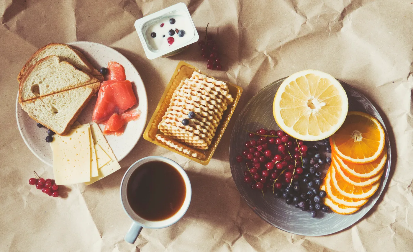 Vue du dessus d'un déjeuner : pain, saumon fumé, fromage, gaufrettes, yogourt aux bleuets, assiette de petits fruits et d'agrumes, tasse de café