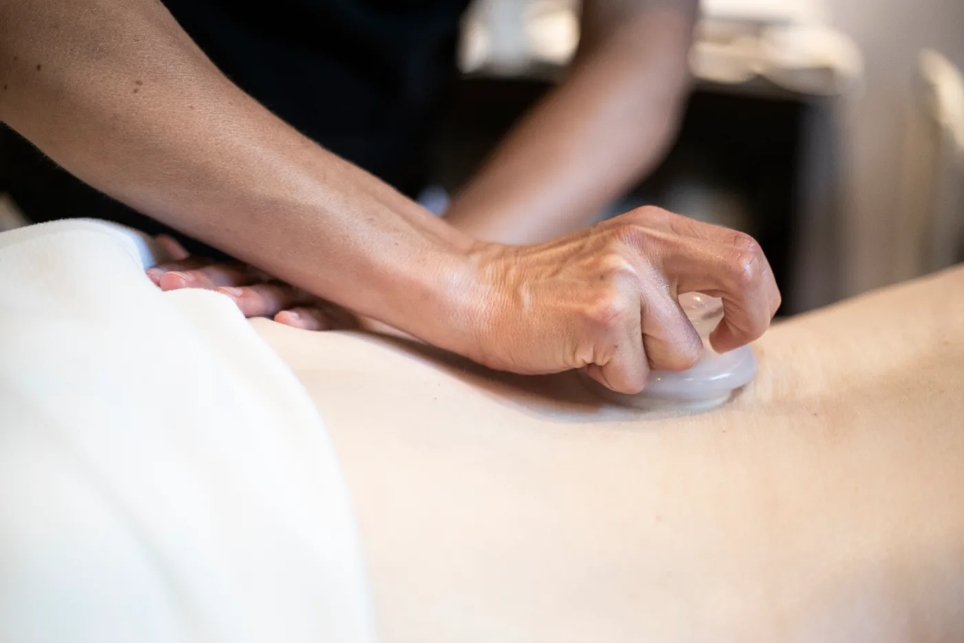 Gros plan : une main tient une ventouse de verre appliquée sur le bas du dos d'une personne couchée